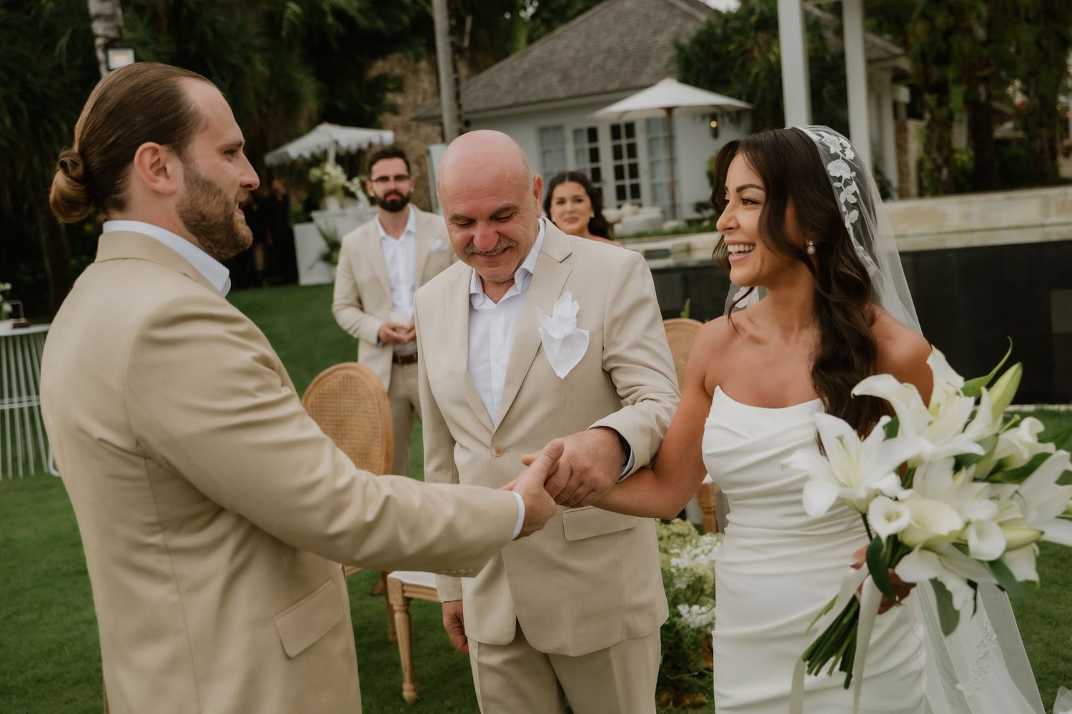 Groom shaking father-in-laws hand as bride arrives smiling at outdoor garden wedding ceremony.