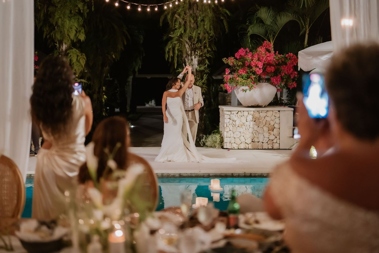 Bride and groom sharing first dance poolside while guests watch at elegant outdoor wedding reception.