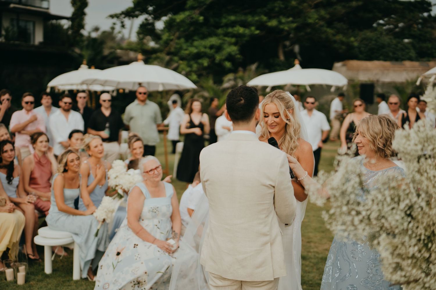 Bride and groom share vows at an outdoor wedding ceremony surrounded by guests.