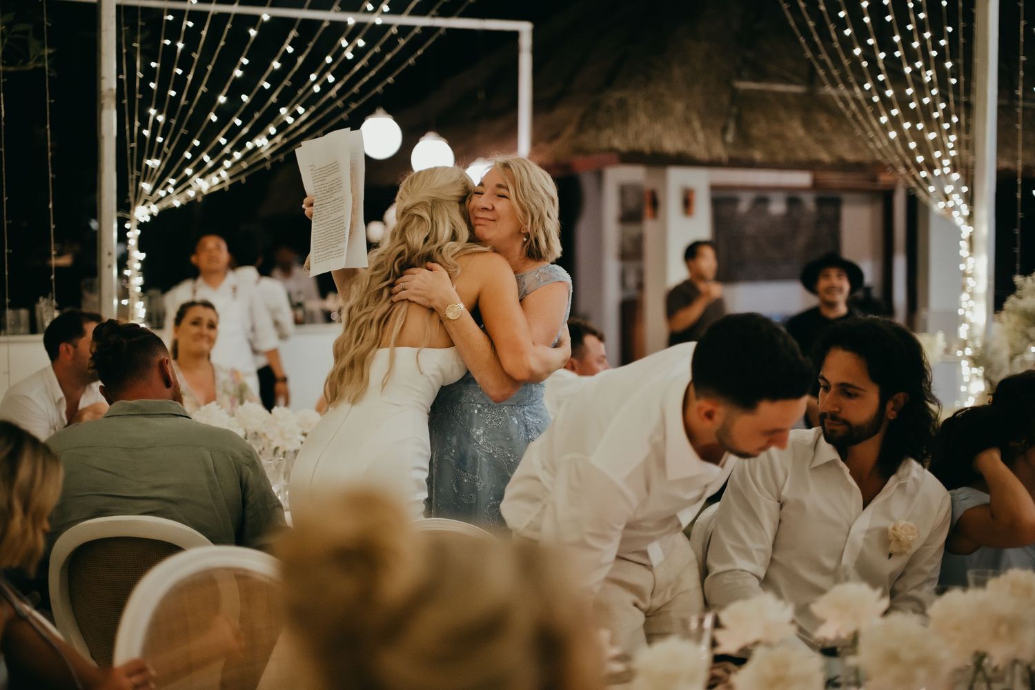 Bride shares a warm embrace with a guest at an elegant fairy-lit wedding reception.