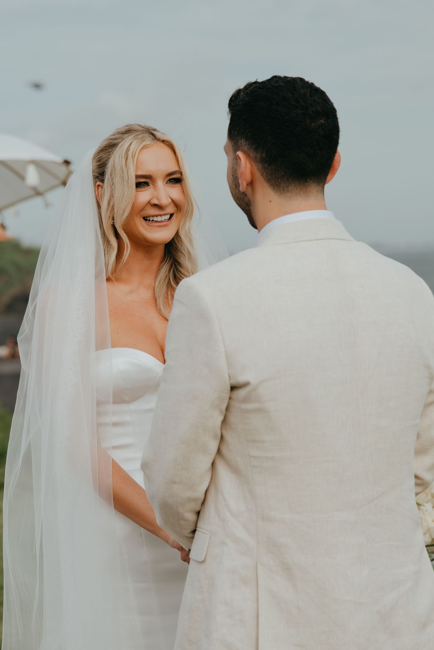 Smiling blonde bride in white strapless gown and veil holding hands with groom at altar.