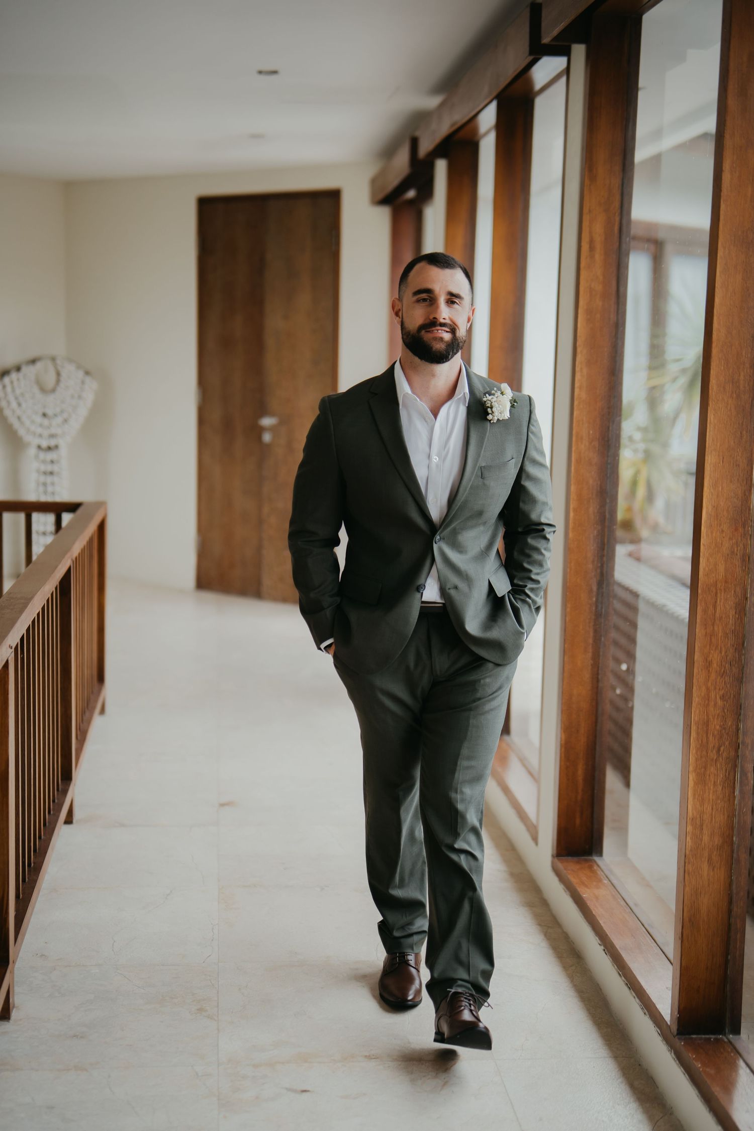 Groom in olive green suit with boutonniere walking down hallway.
