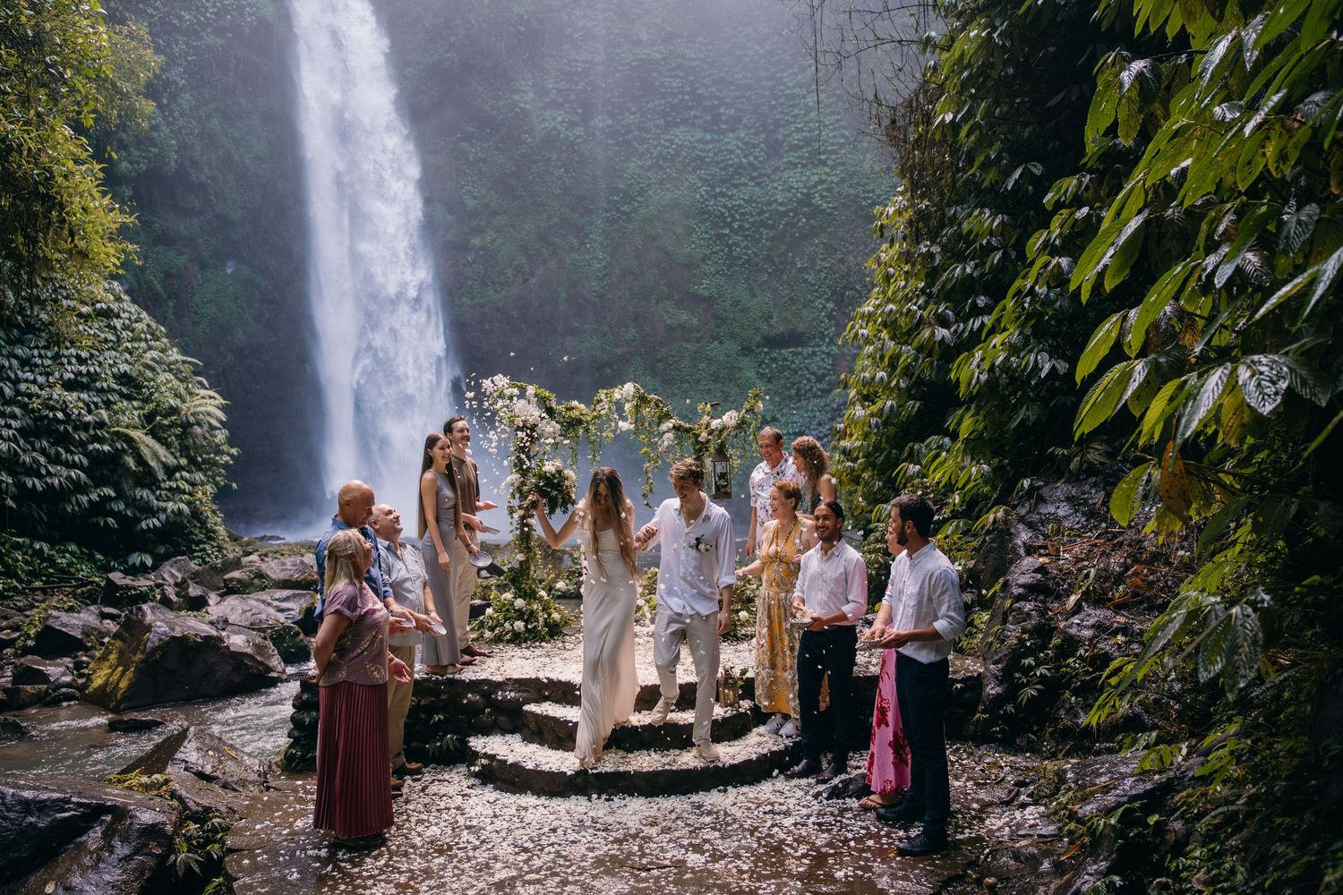People gather at a scenic waterfall viewpoint in a lush forest setting, creating a panoramic view of nature's beauty.