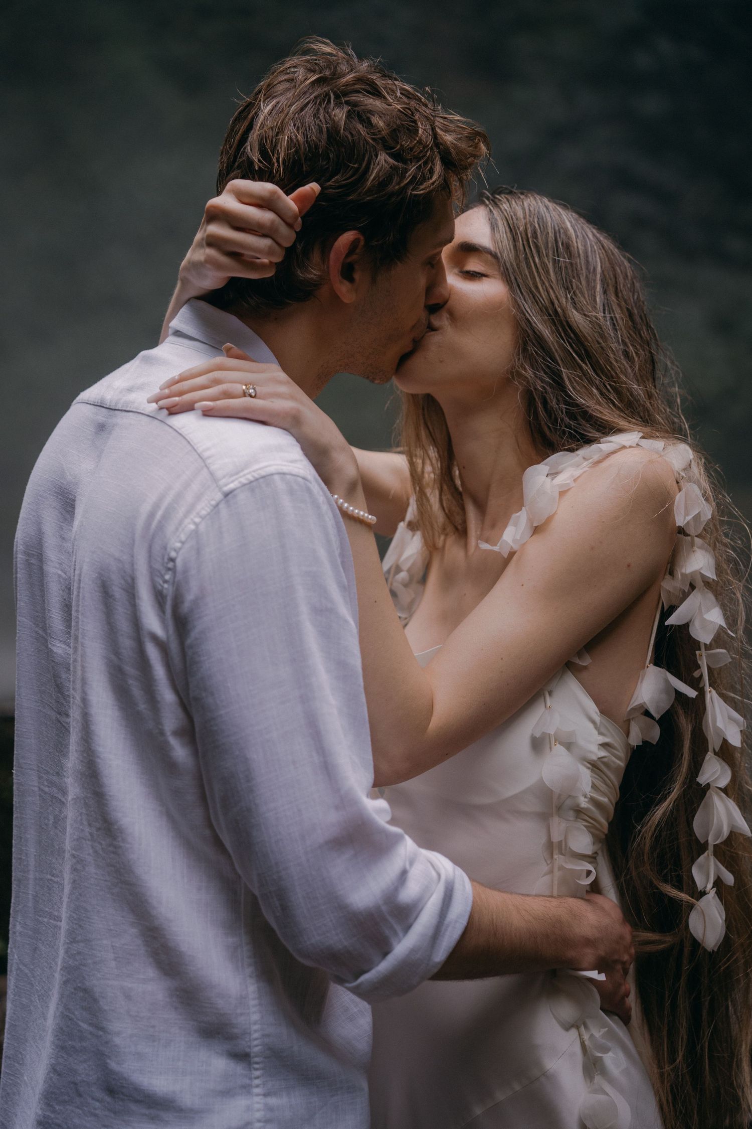 A romantic couple in wedding attire share an intimate kiss against a moody dark background.