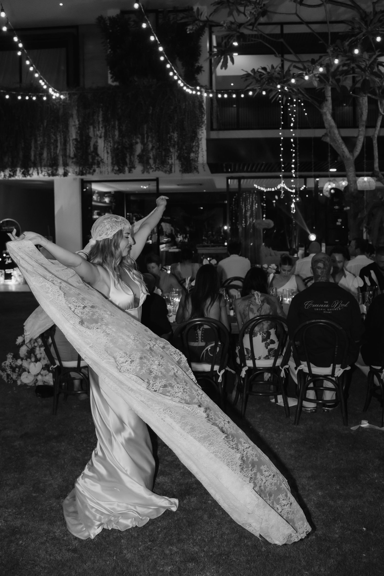 Black and white photo of bride twirling her lace wedding gown train at an outdoor evening reception.