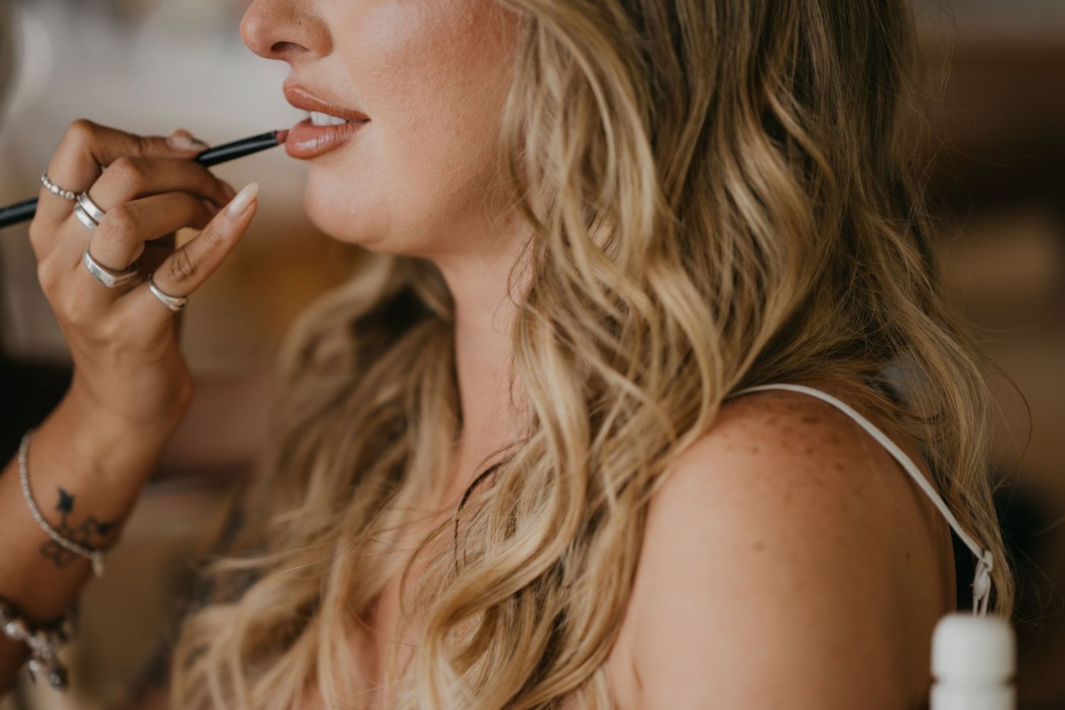 Close-up of blonde bride having lipstick applied by makeup artist on her wedding day.