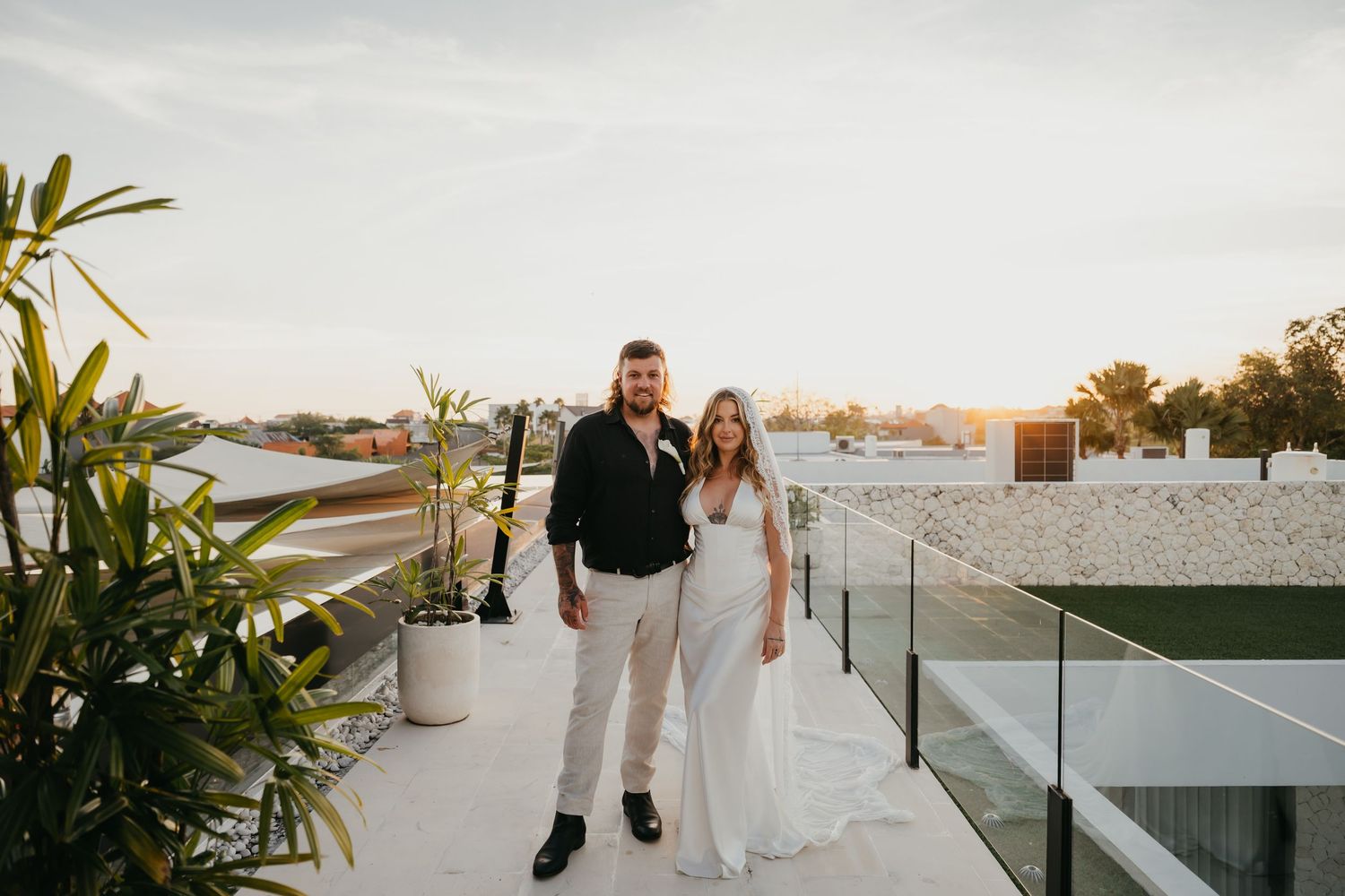 Bride and groom pose together on a rooftop terrace at sunset with a modern villa backdrop.