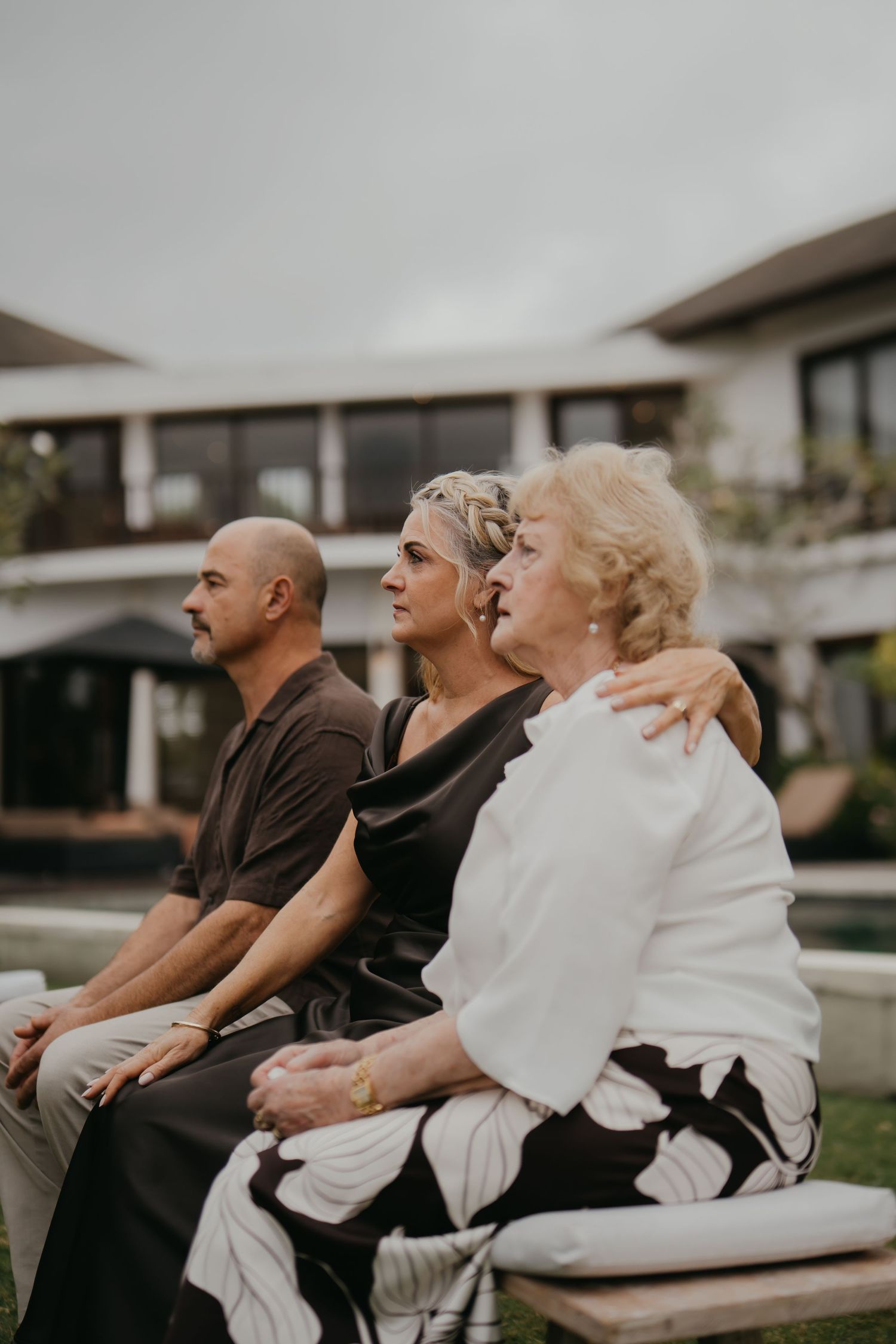 Wedding guests including elderly woman in white seated outdoors at intimate garden ceremony.