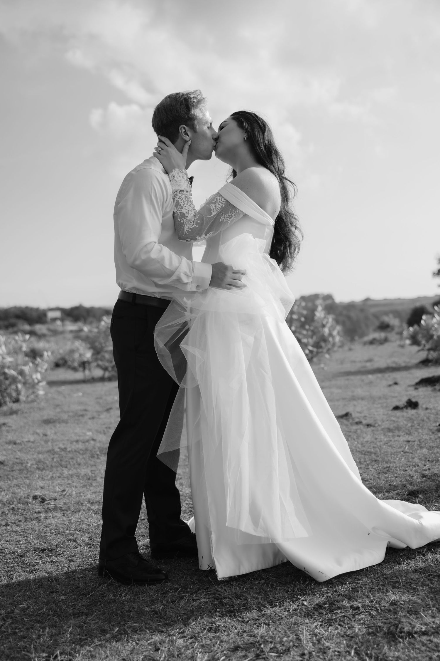 Black and white photo of bride and groom sharing a romantic kiss outdoors on their wedding day.