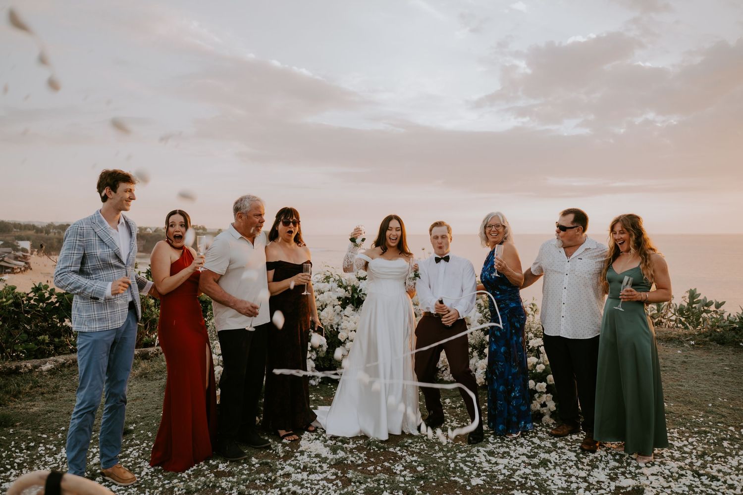 Wedding party group photo with bride and groom at a cliffside sunset ceremony.