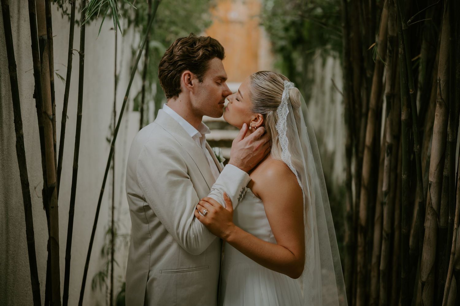Newlywed couple sharing a romantic intimate moment surrounded by bamboo in wedding attire.