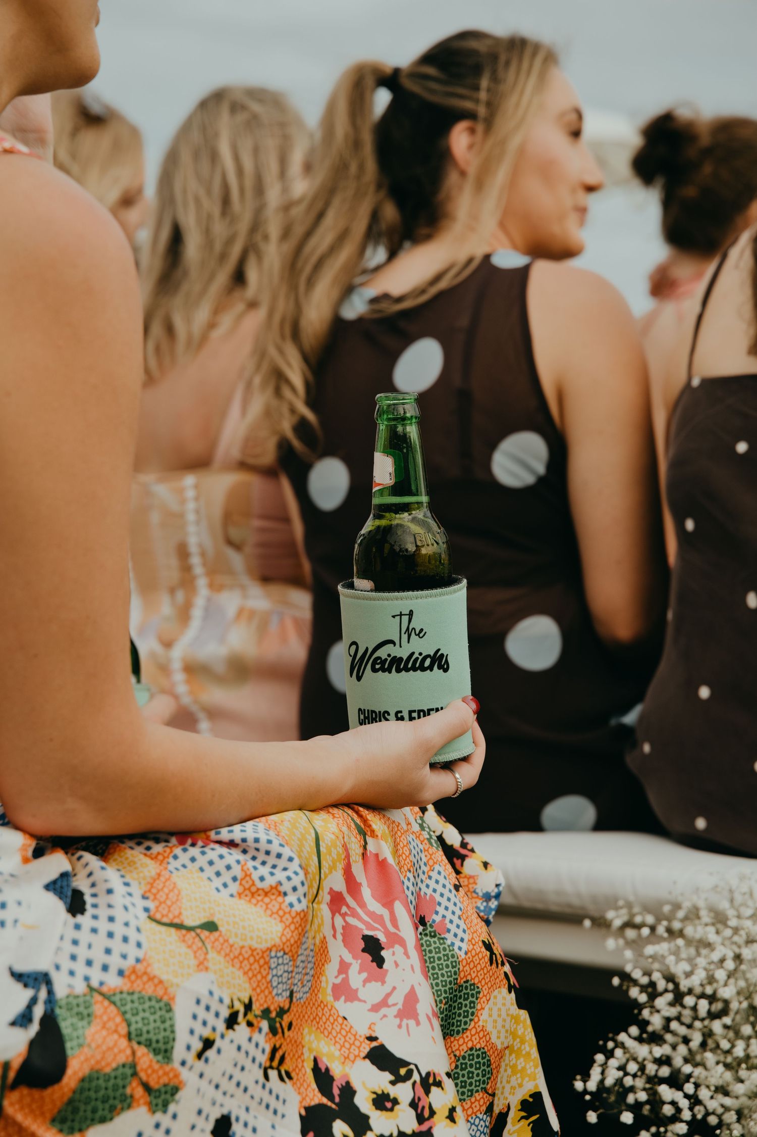 Wedding guest holding a custom beer koozie reading The Weinlicks at an outdoor celebration.