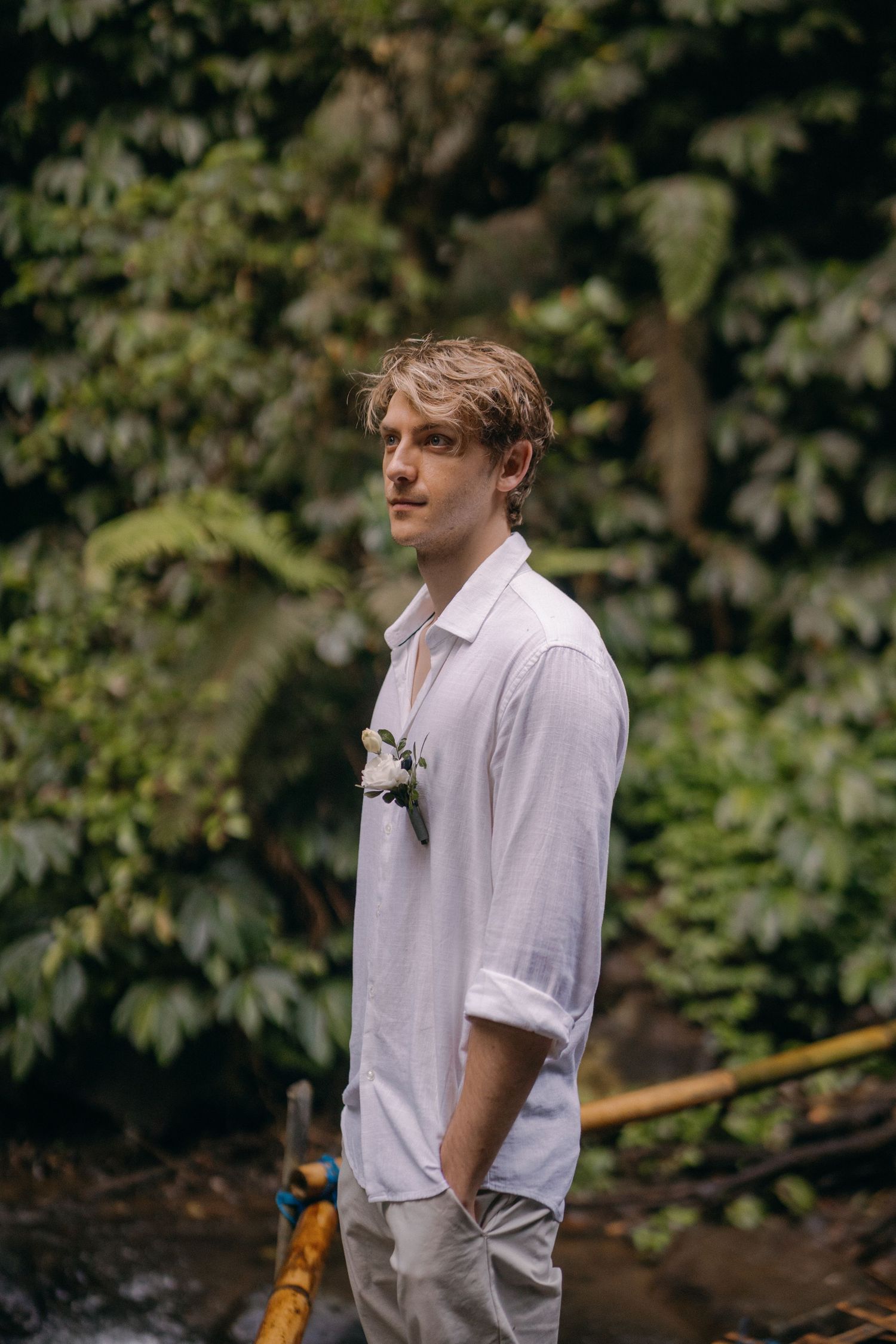 Person in white button-down shirt standing outdoors against green foliage background.