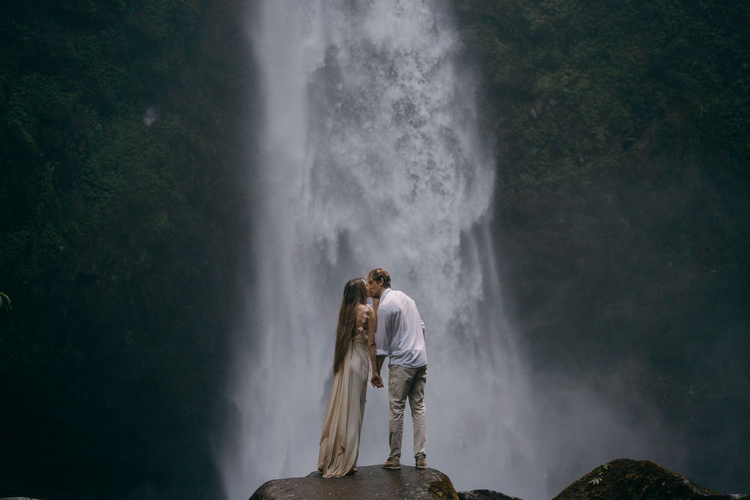 A couple stands together in silhouette against a misty waterfall backdrop creating a romantic atmosphere.