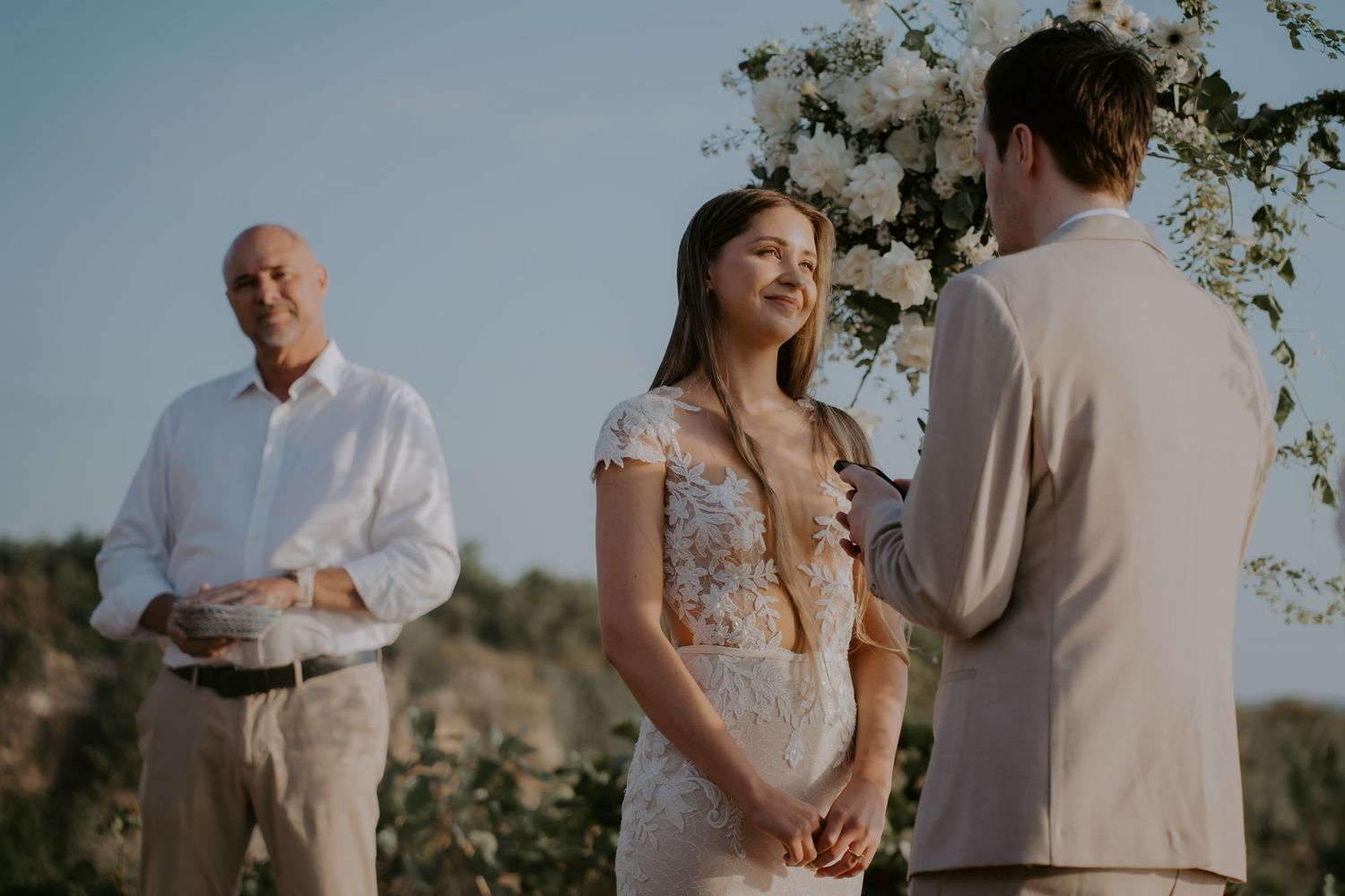 Romantic outdoor wedding ceremony with couple exchanging vows under blooming trees in golden sunlight.
