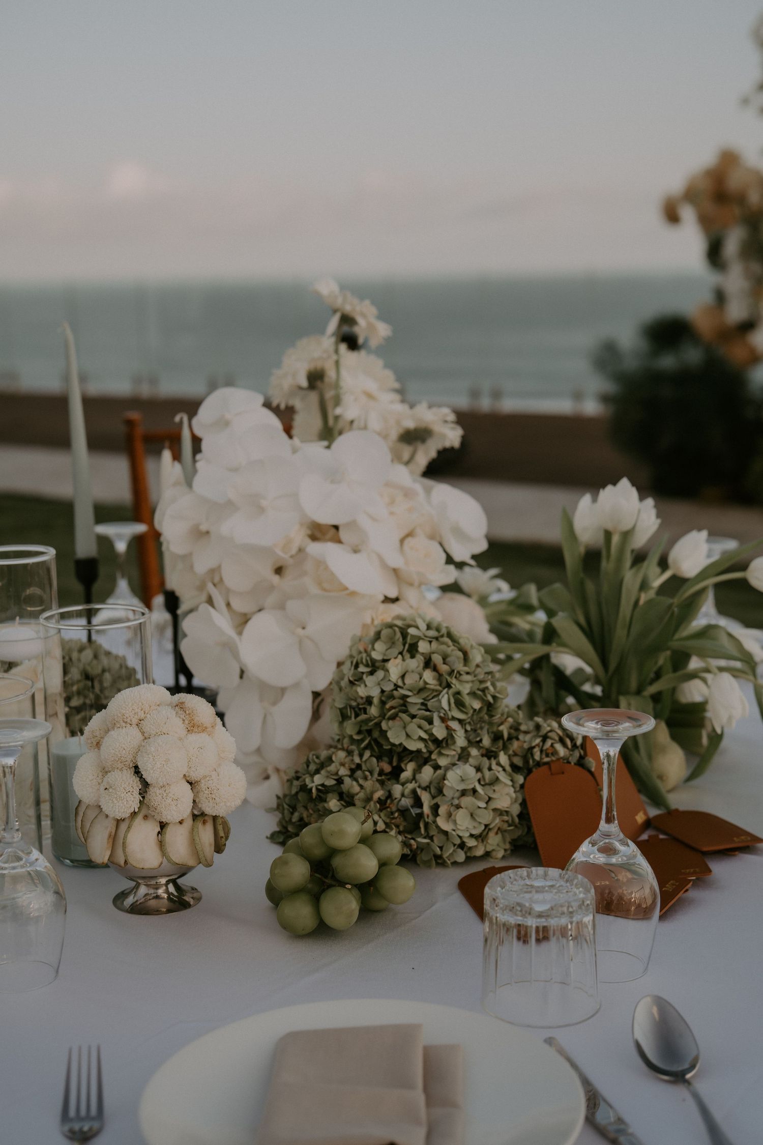 White orchid and hydrangea floral centerpieces adorn an elegant table setting at a beachside wedding reception.