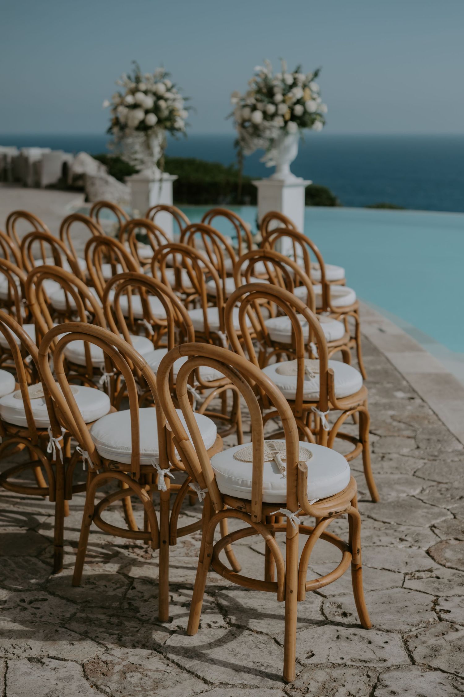 Wooden cross-back chairs with white cushions set up for an oceanfront ceremony.
