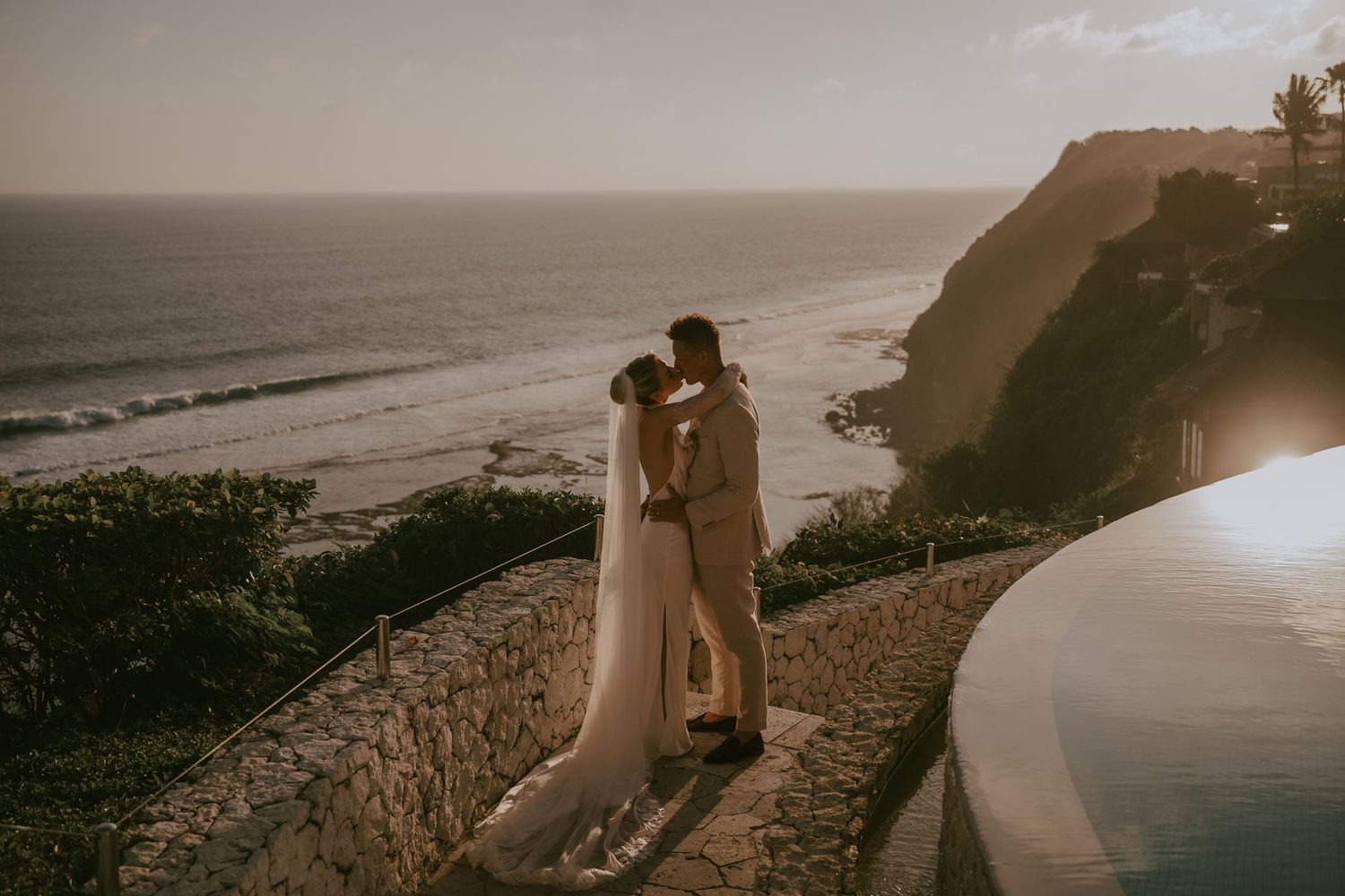 Romantic seaside wedding photoshoot with stone wall and ocean backdrop.