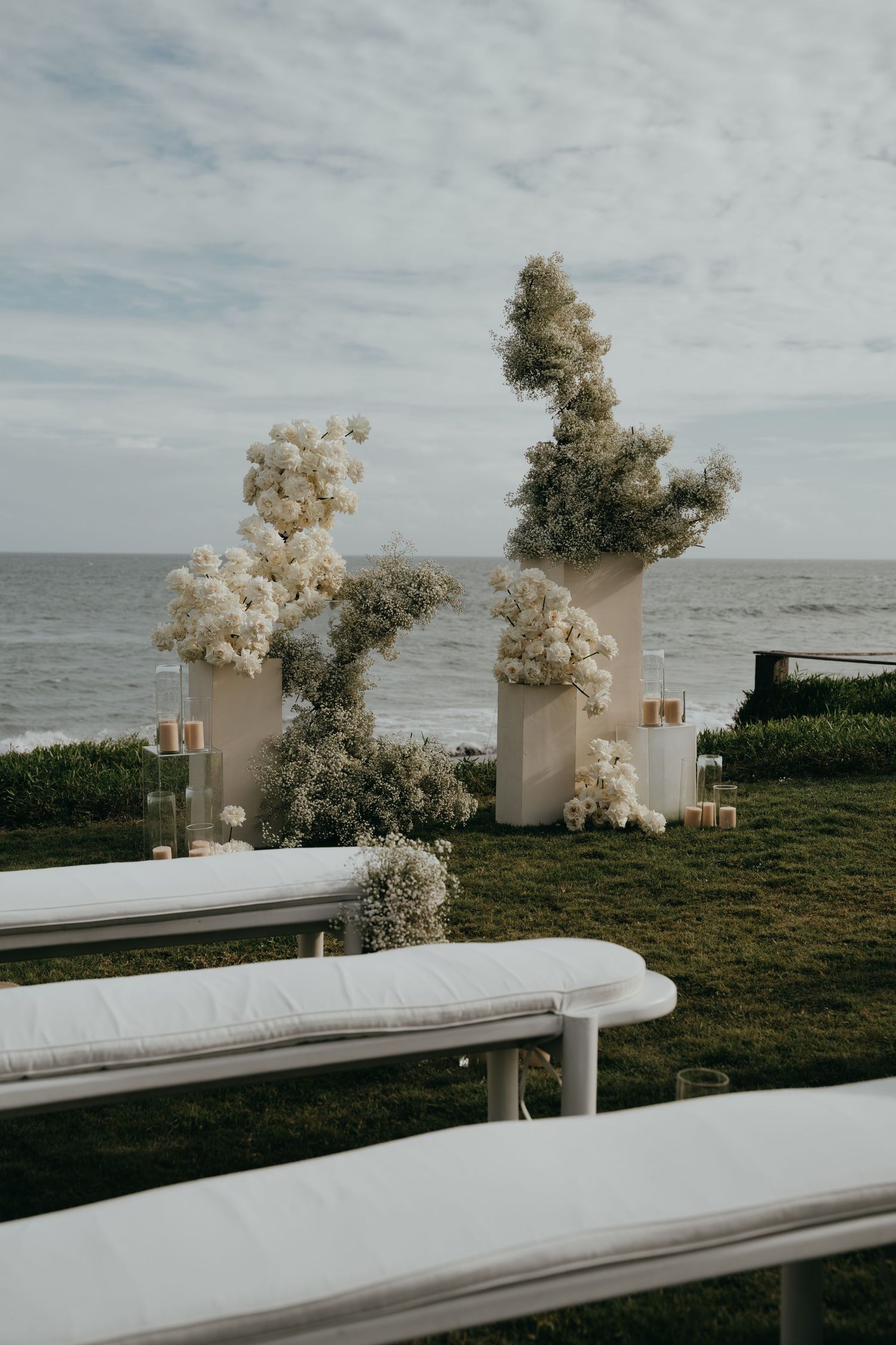 Outdoor beach wedding ceremony setup with white floral arrangements and white benches.