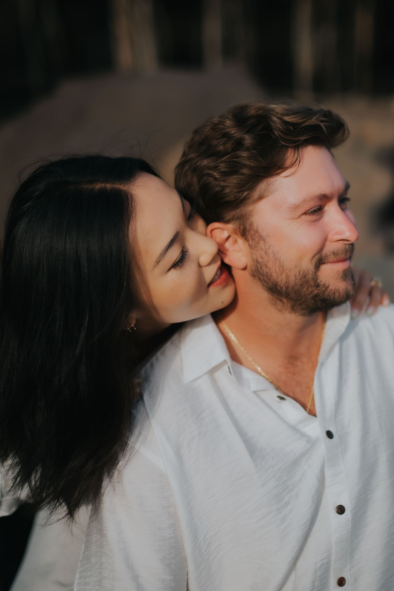 Romantic couple in white shirts share an intimate moment during a warm sunset photoshoot.