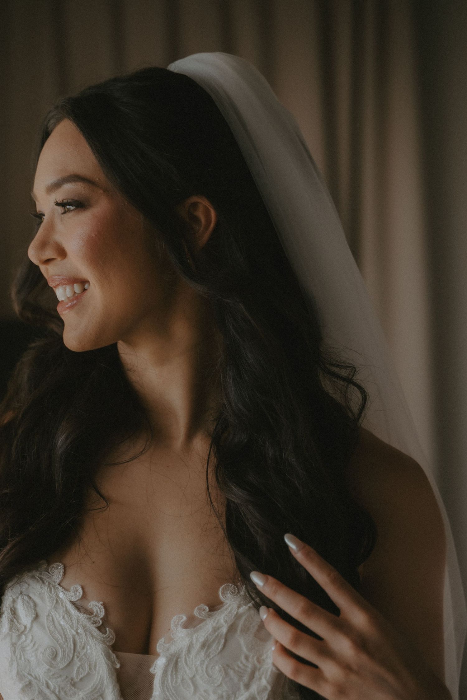 A bride in a white lace wedding dress looks down with a soft smile in a series of moody, intimate portraits.