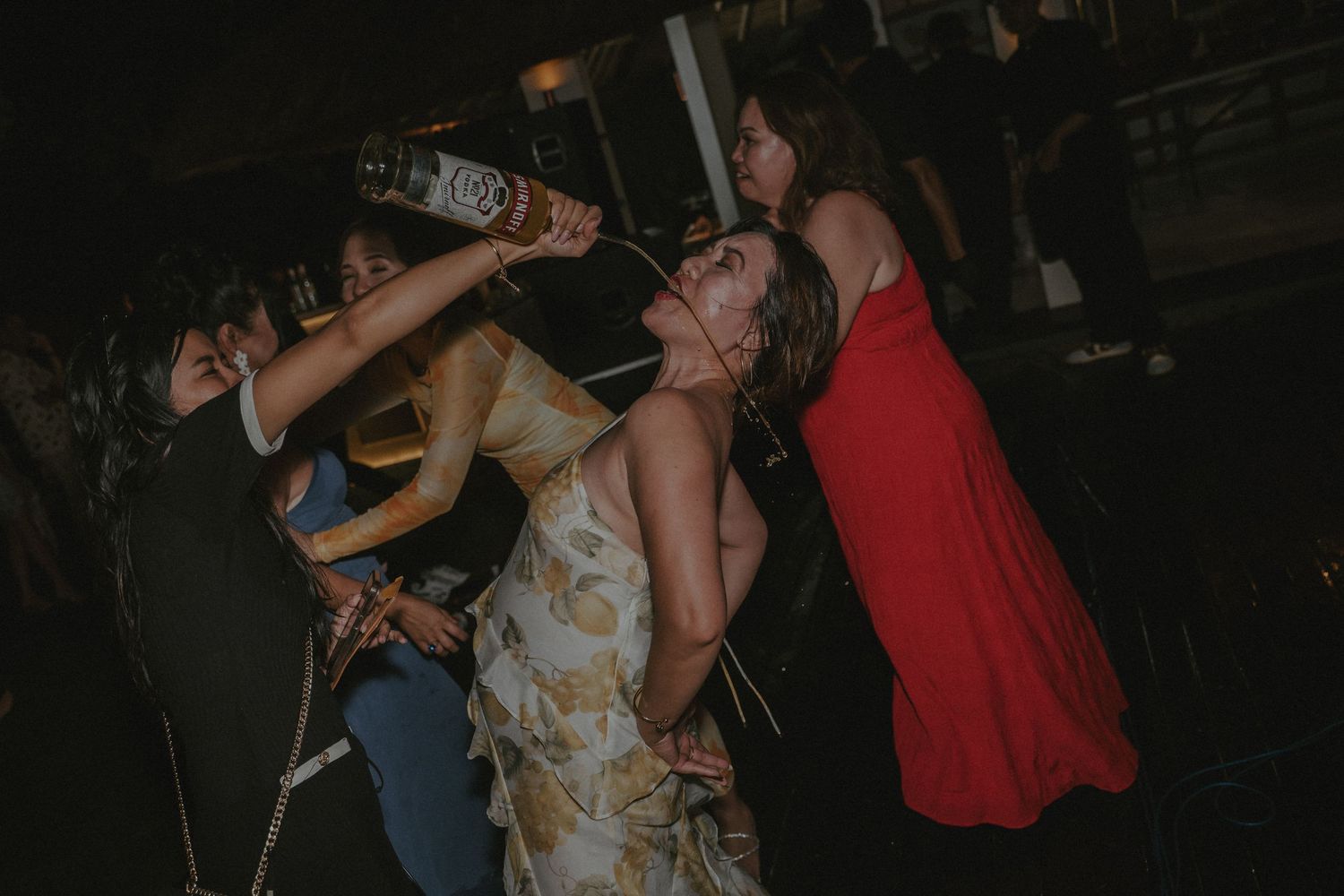 Group of people drinking from bottles at a party in a dark setting.