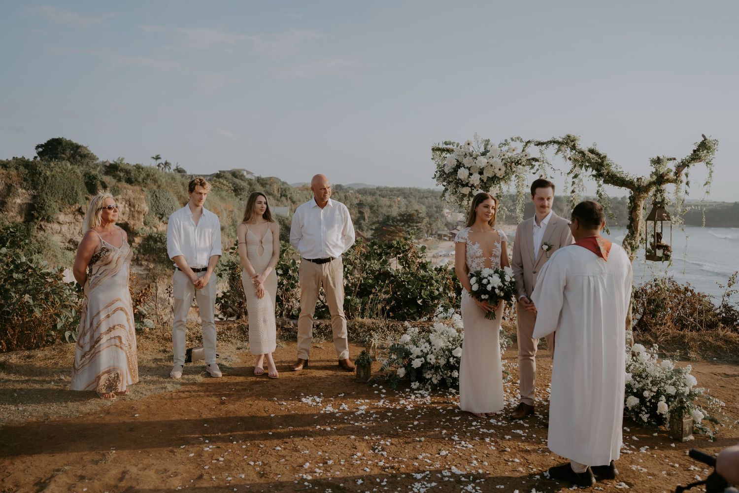 A romantic outdoor wedding ceremony in a desert setting with floral arrangements and guests gathered at sunset.