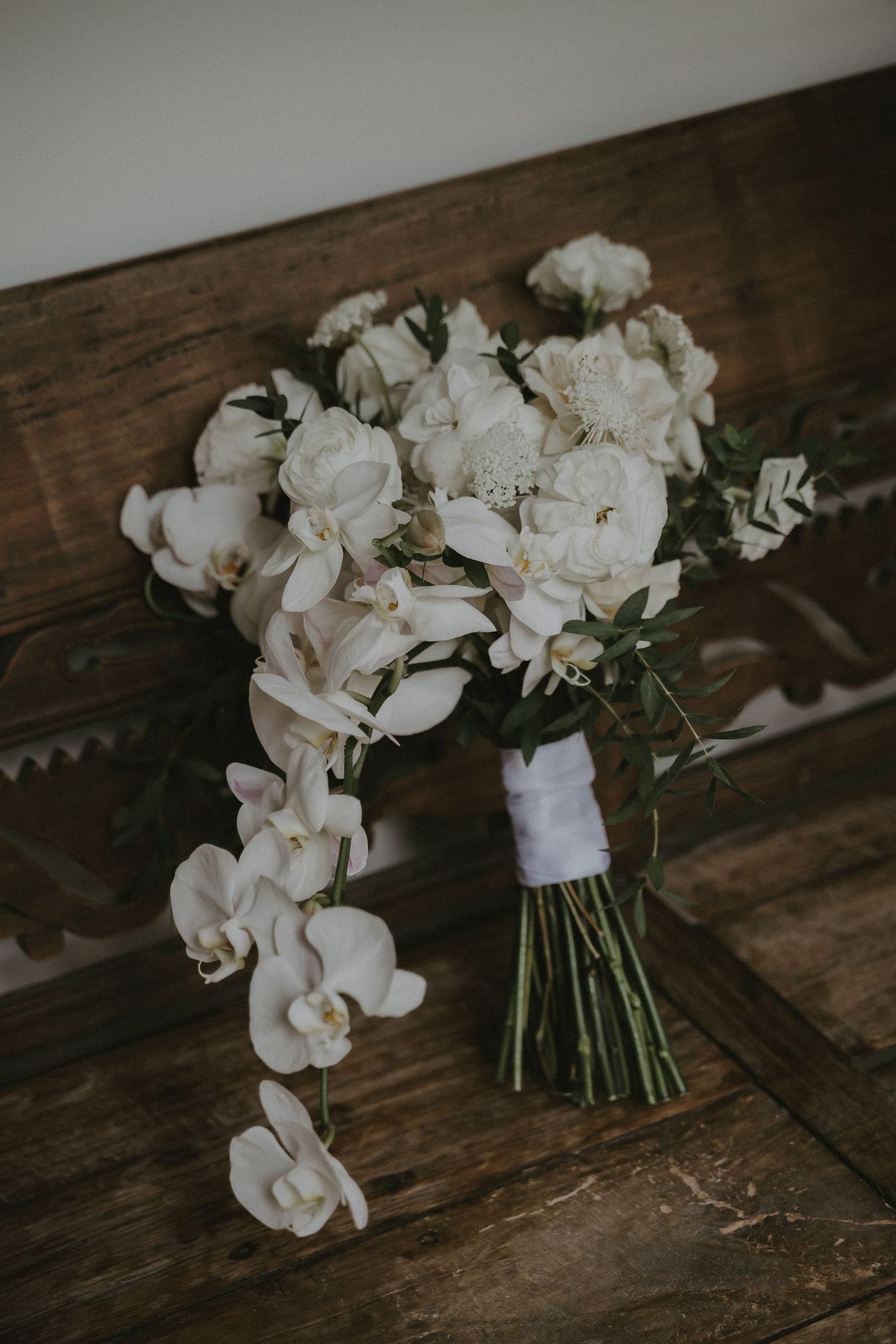 Elegant white orchid and rose wedding bouquet displayed on rustic wooden surface.