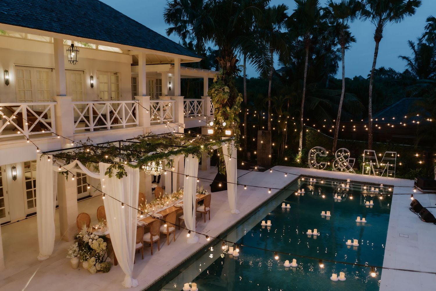 Stunning tropical wedding venue at dusk with pool, string lights, and elegant outdoor dining setup.