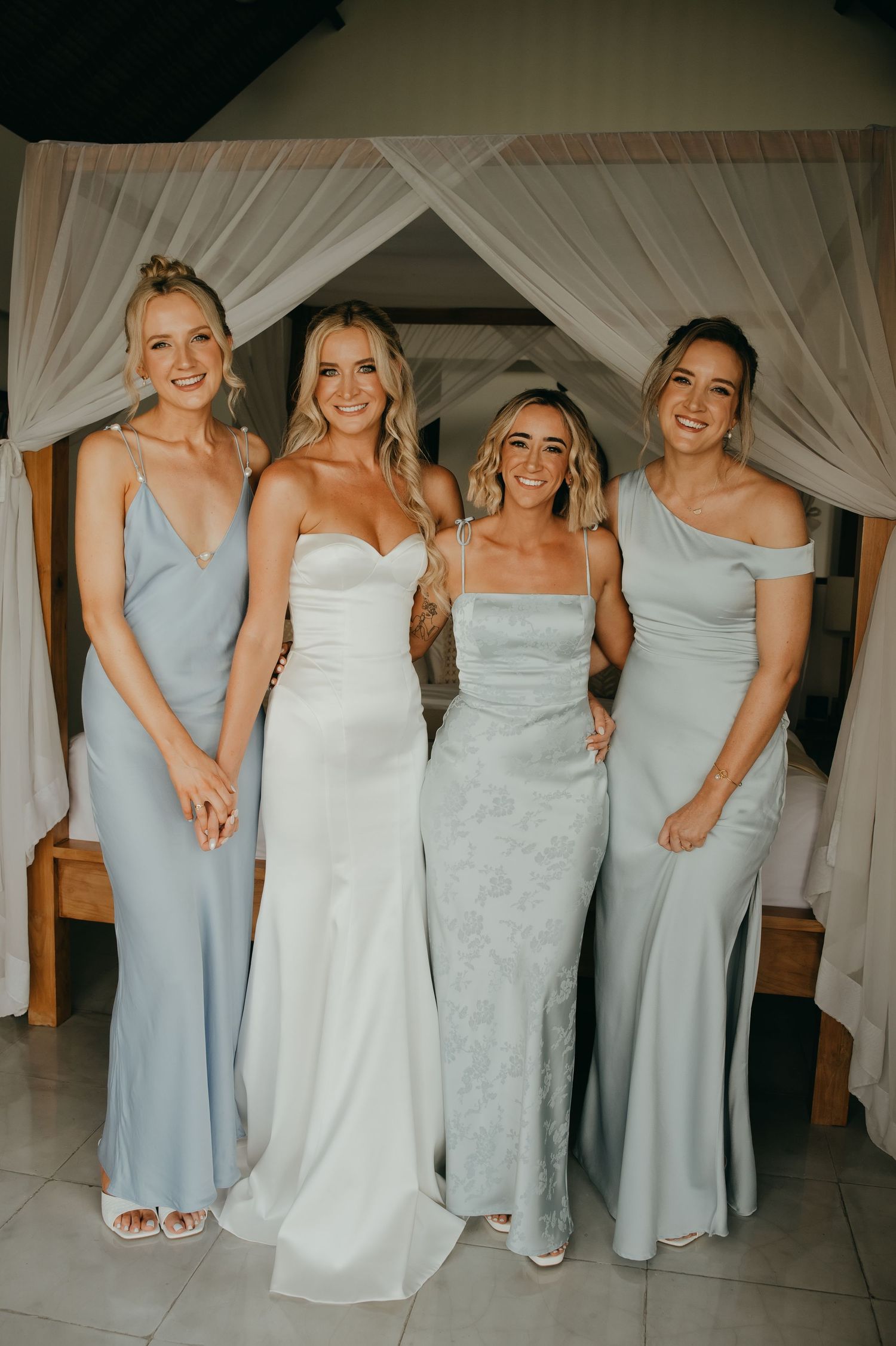 Bride in white gown posing with three bridesmaids in light blue dresses inside elegant venue.