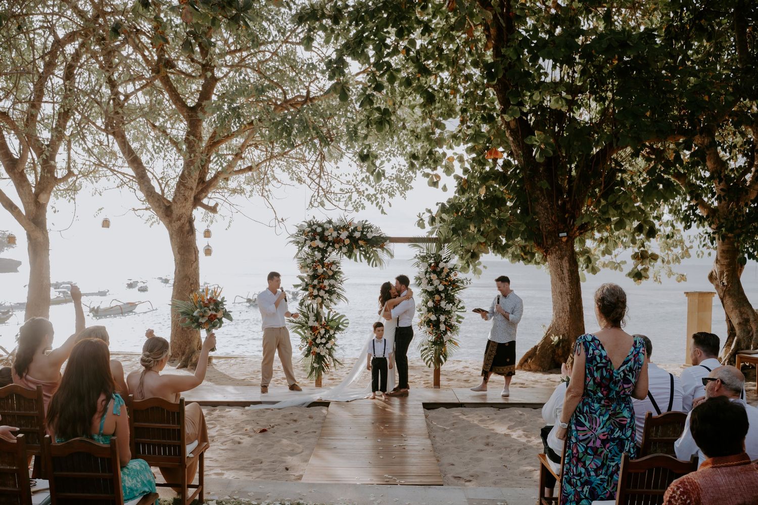 A group of people gather outdoors under trees during a casual event in natural lighting.
