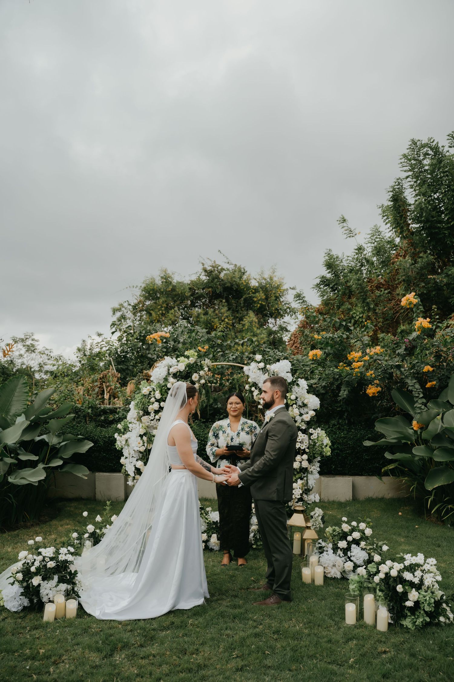 Bride and groom exchange vows under floral arch with candles at outdoor garden wedding.