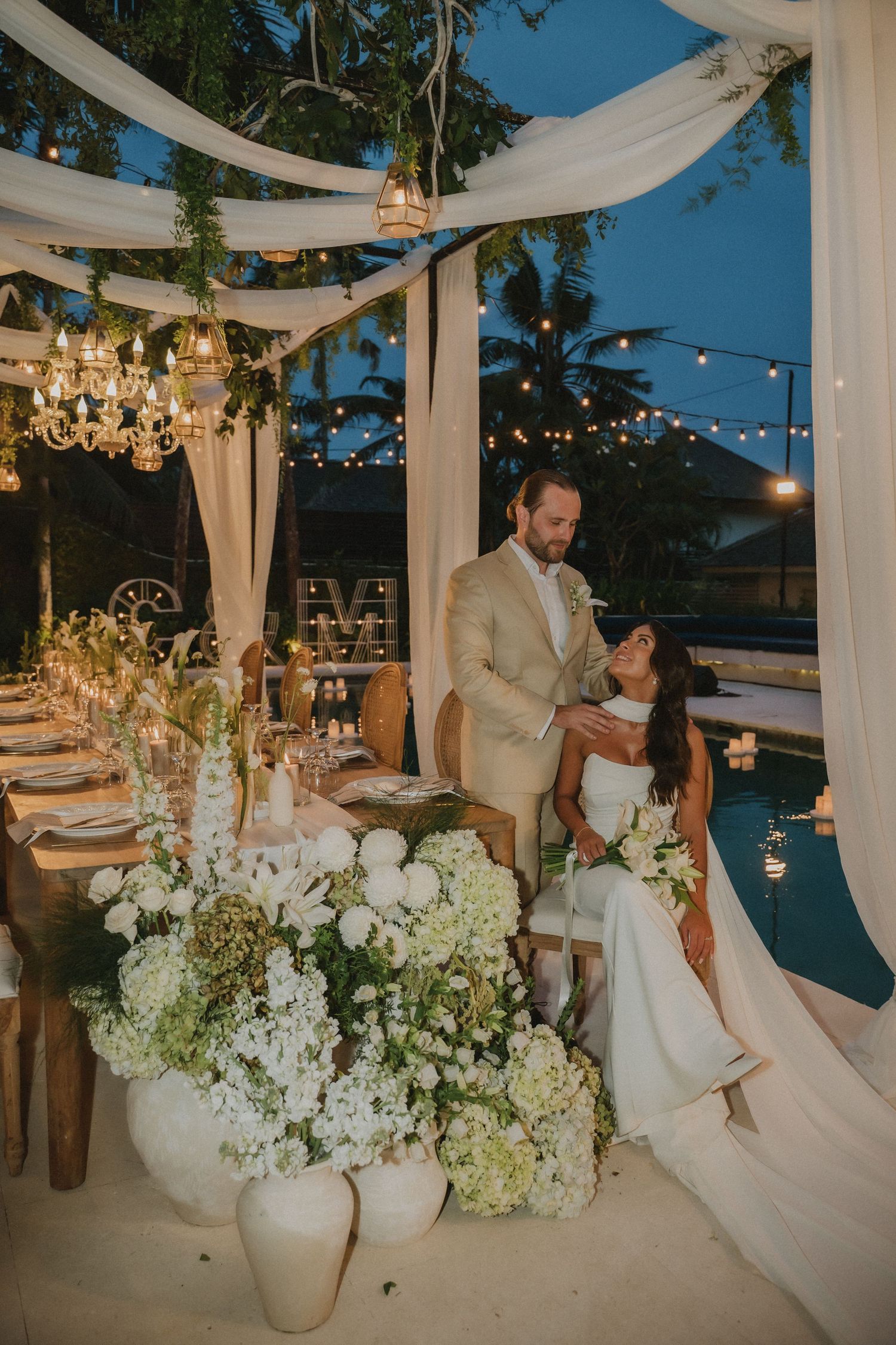 Bride and groom share a romantic moment at candlelit wedding reception table adorned with white hydrangeas.