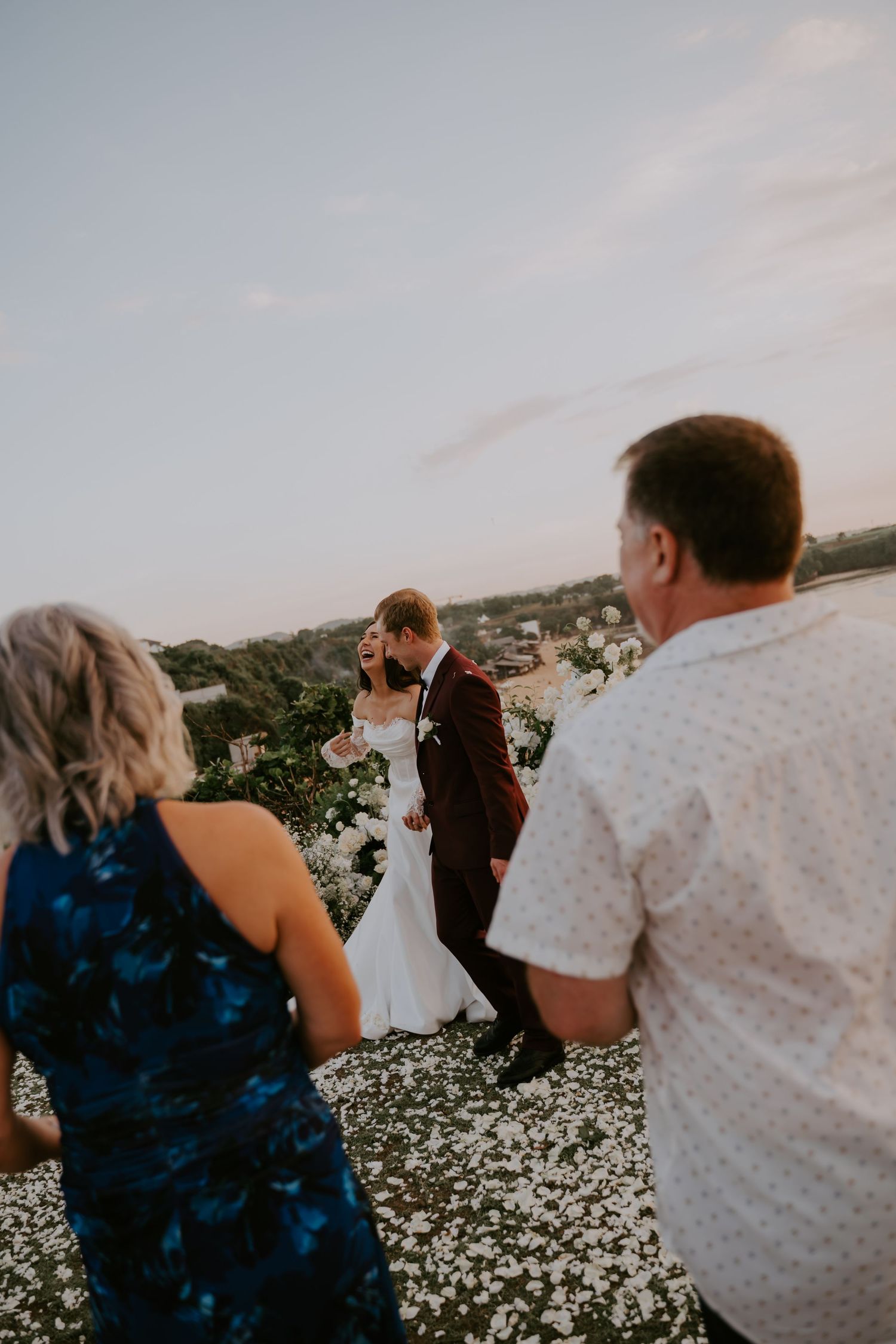 Newlyweds walk back down the aisle through flower petals as guests celebrate after outdoor wedding ceremony.