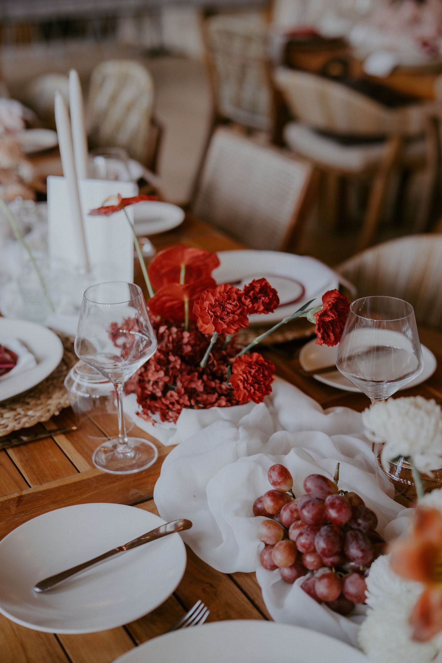 Elegant wedding reception table with red florals, grapes, white candles, and glassware.