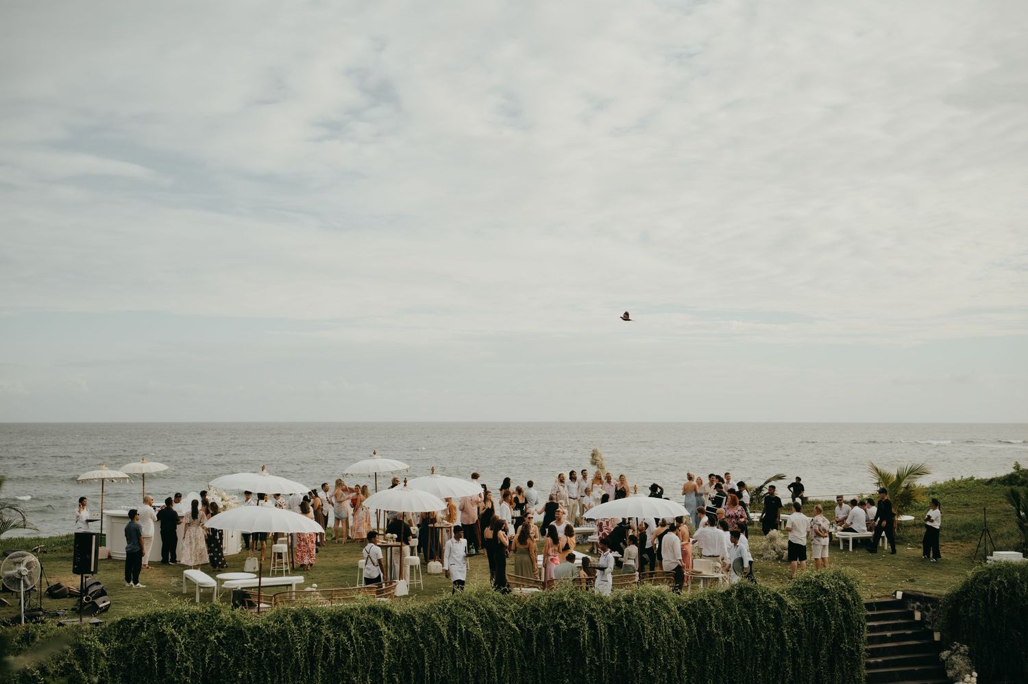 Aerial view of wedding cocktail hour on a cliff overlooking the ocean with white umbrellas.