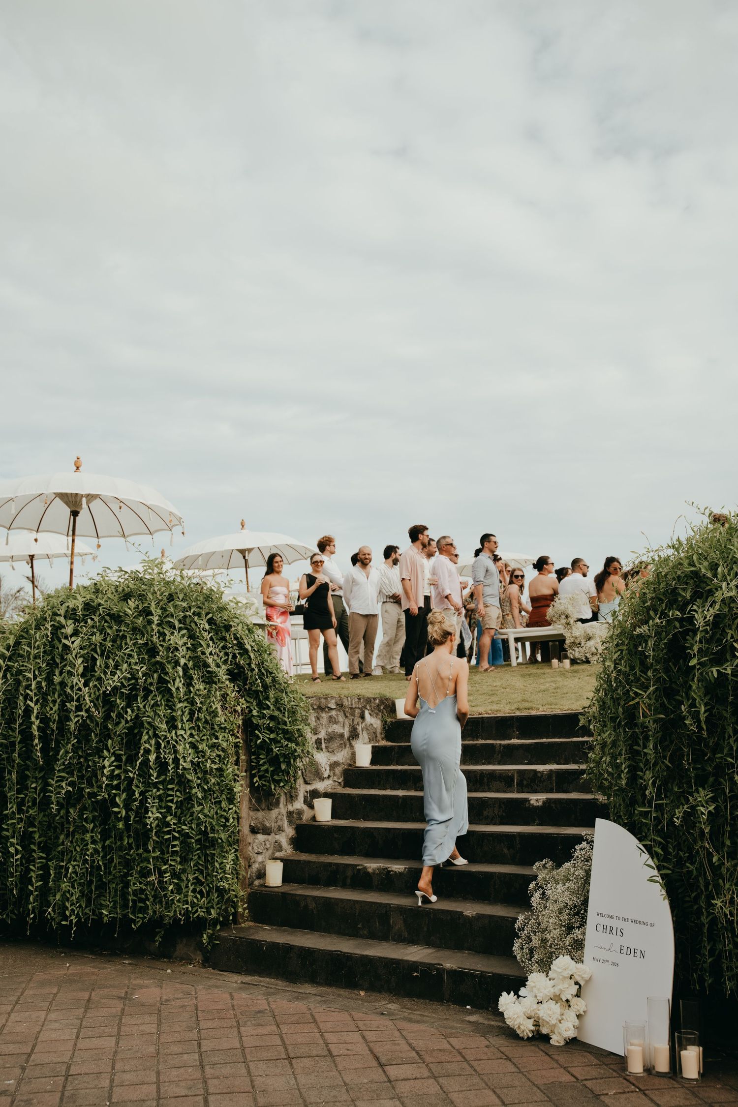 Wedding guests gathering on a clifftop terrace, ascending stone steps lined with candles and greenery.