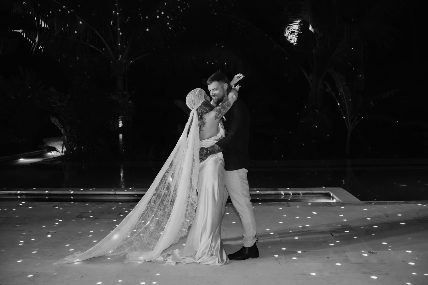 Black and white photo of bride and groom sharing first dance under starry night sky.