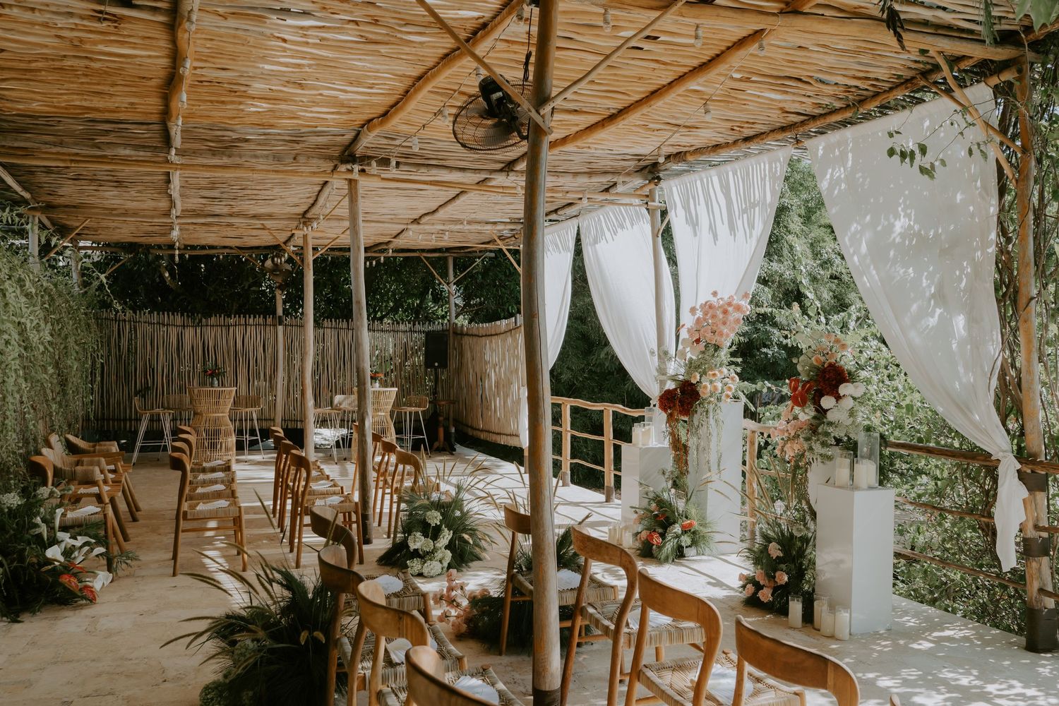 Rustic bamboo wedding ceremony venue with wooden chairs and floral arrangements in tropical garden setting.