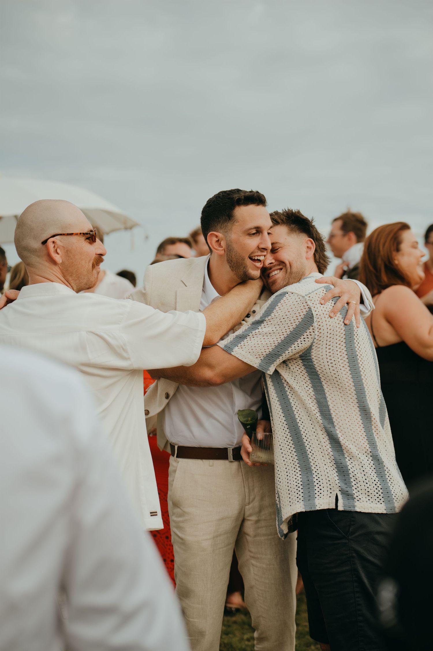 Groom embraces a guest in a warm congratulatory hug following an outdoor tropical wedding ceremony.