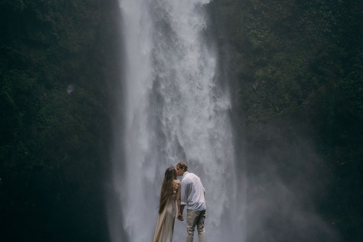 Majestic waterfall cascades down a rocky cliff face in a lush green forest setting.