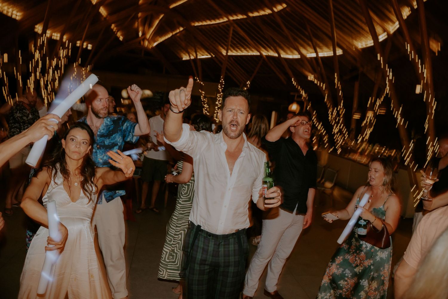 People dancing and celebrating at a dimly lit wedding reception with warm lighting and festive atmosphere.