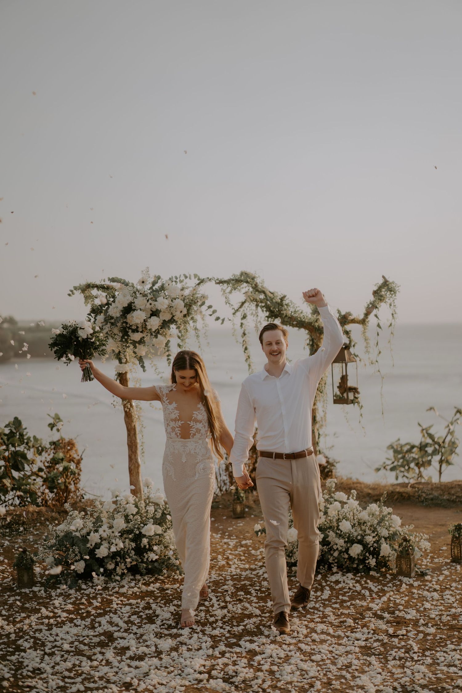 A couple walks together on a scenic beach path decorated with floral arrangements at sunset.