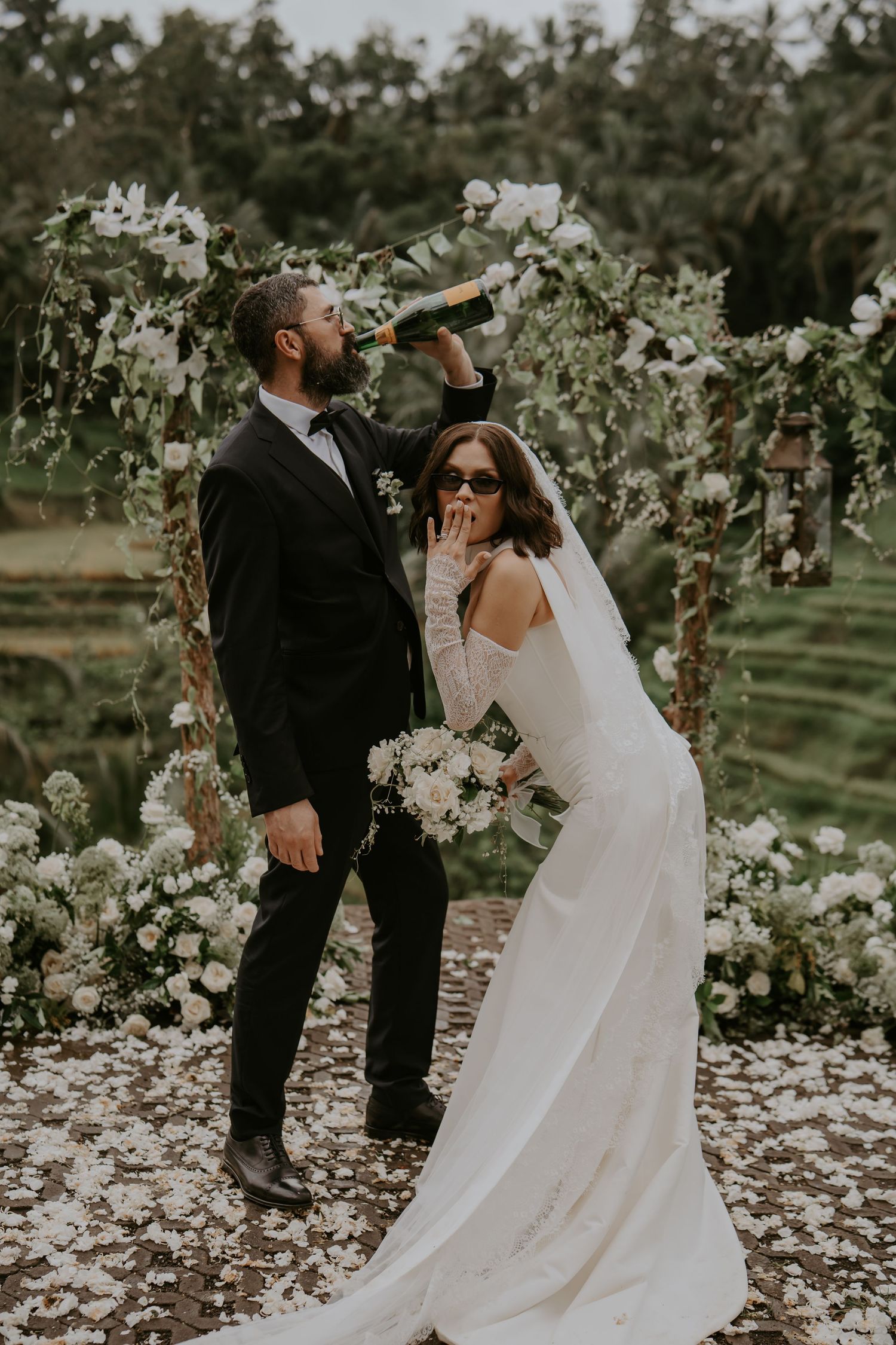 Newlyweds share intimate moments in a dreamy outdoor setting with white floral decorations.