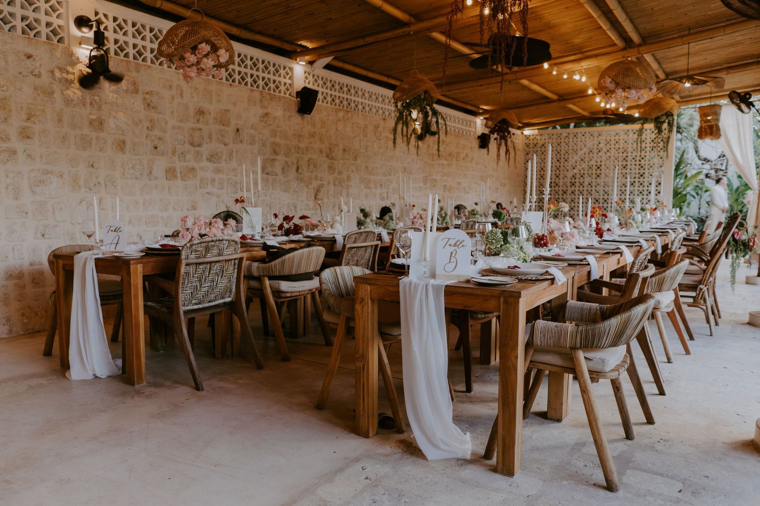 Rustic wedding reception with long wooden tables, wicker chairs, and elegant floral centerpieces.