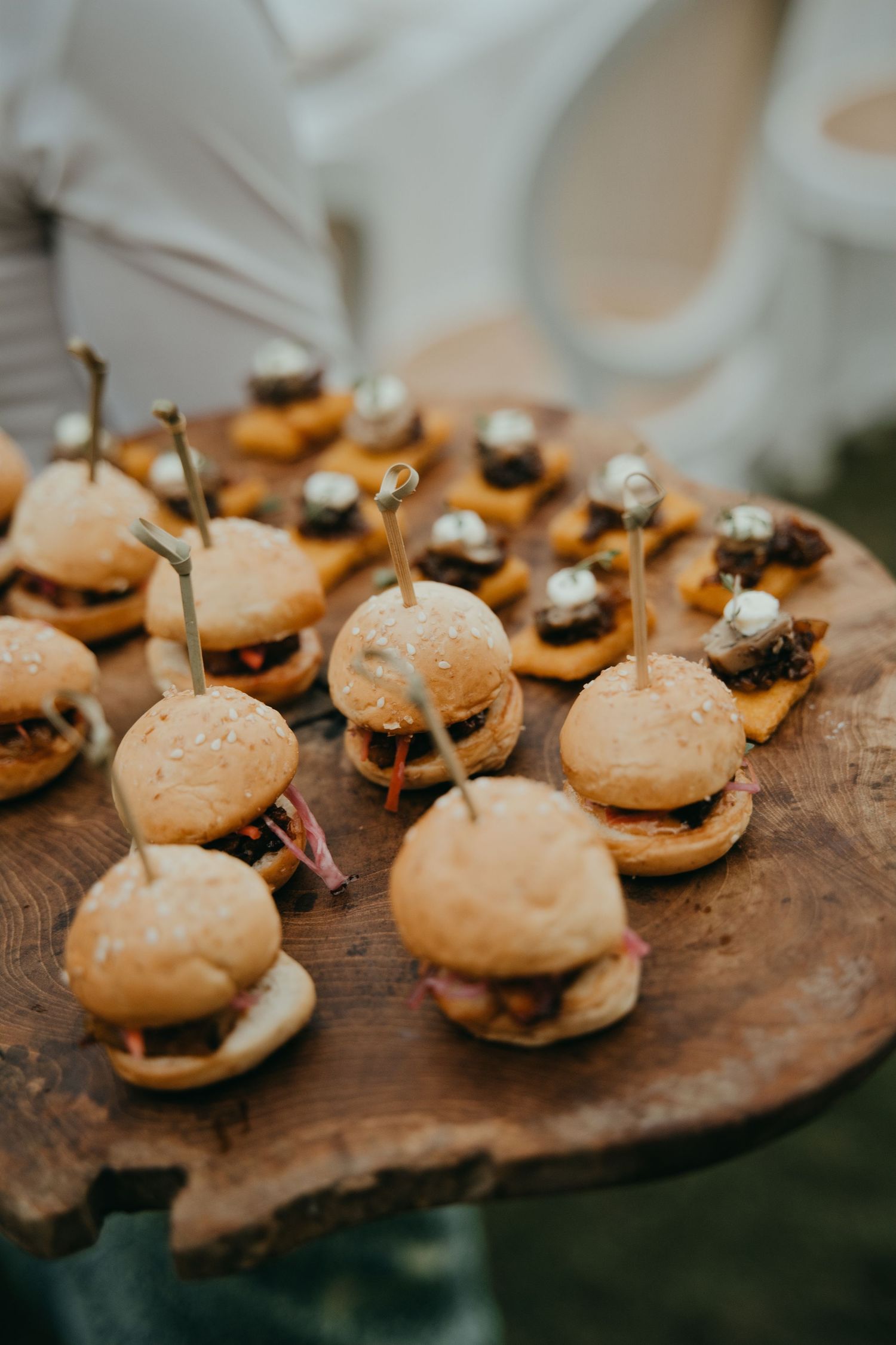Assorted mini sliders served on a rustic wooden board at a wedding reception catering display.