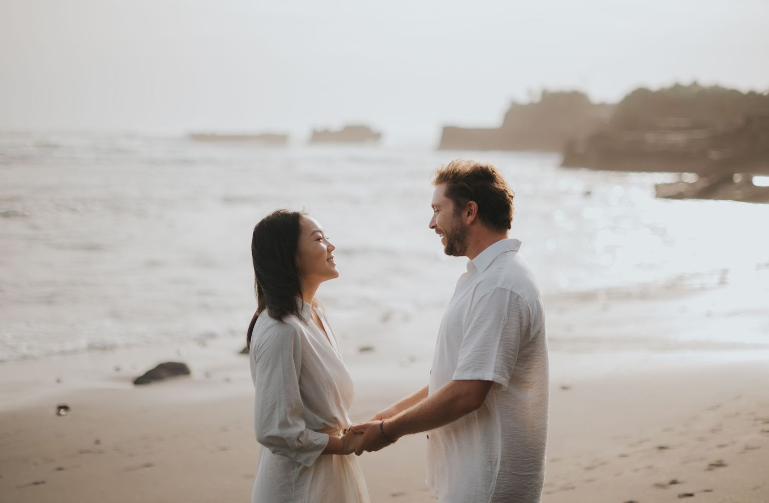 A couple walks along a misty beach shore holding hands in romantic black and white photos.