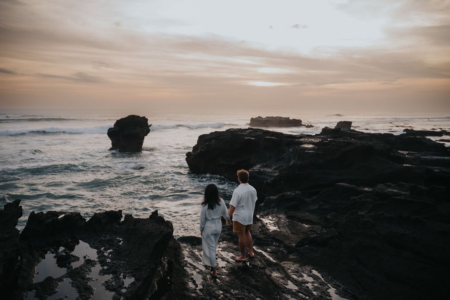 Scenic coastal landscape with dark rocky cliffs against a moody sunset sky over the ocean.
