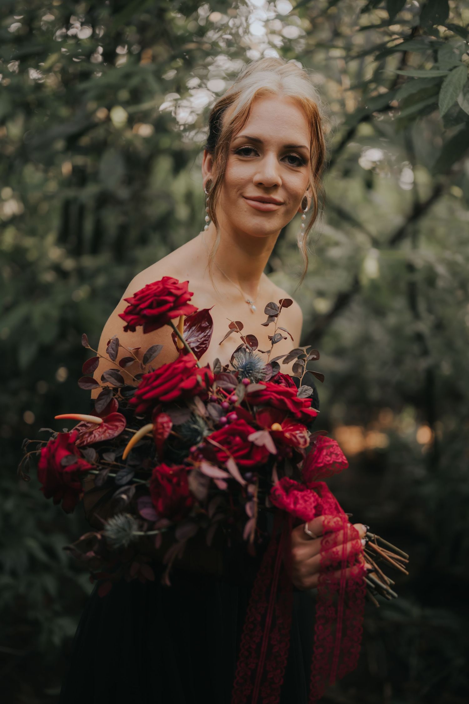 A bouquet of deep red and burgundy flowers against a moody forest background.