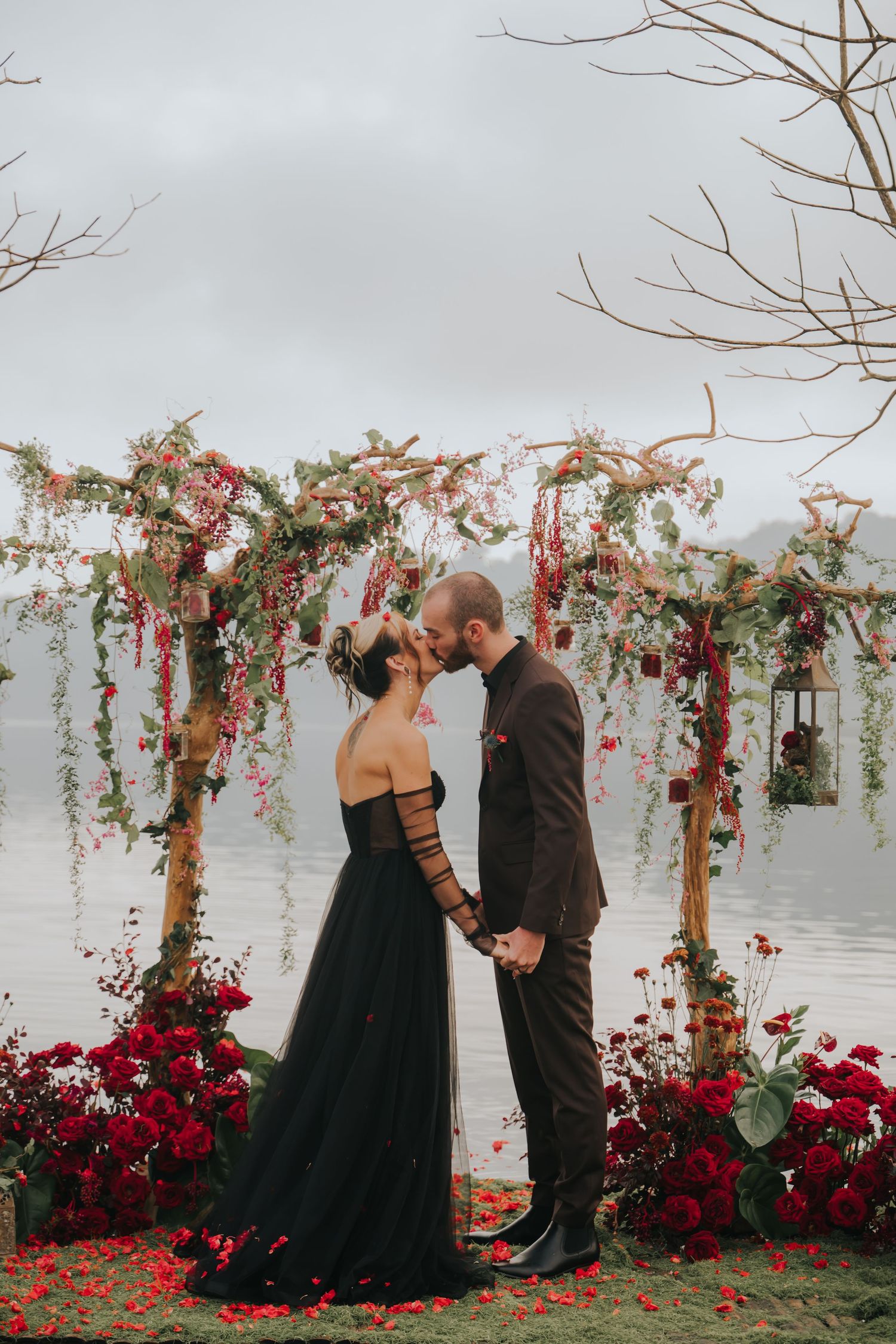 A romantic wedding ceremony setup with a floral arch and deep red roses against a white wall.